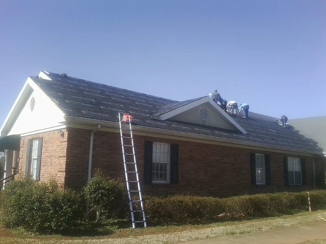 Crew tearing shingles off a brick ranch roof with a ladder set — Emergency Roof Repair work by our crew in Linwood